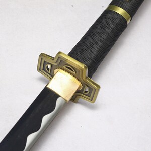 A close-up of the katana's hilt, showing a black textured grip, a gold square guard, and part of the silver blade.