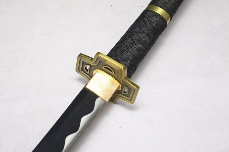 A close-up of the katana's hilt, showing a black textured grip, a gold square guard, and part of the silver blade.