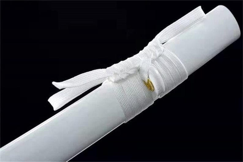 Close-up of a white katana scabbard with a white cord wrapped around it, secured by a small gold-colored ring.