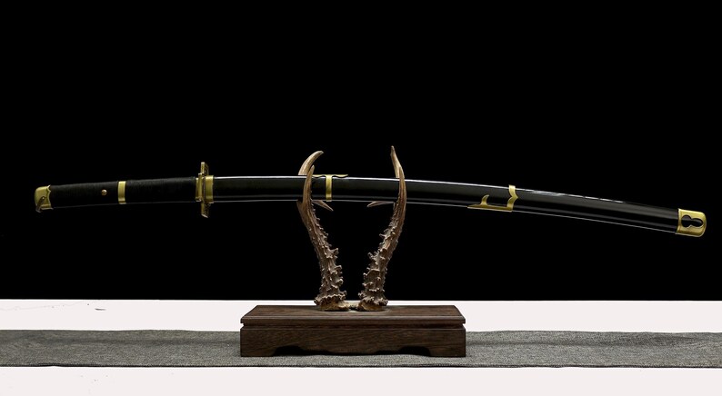 A black and gold katana scabbard with gold accents rests on a wooden stand with antler-like supports.