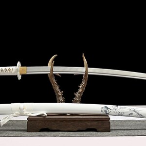 A white katana sword with a white hilt and a white scabbard with a geisha design rests on a wooden antler stand.