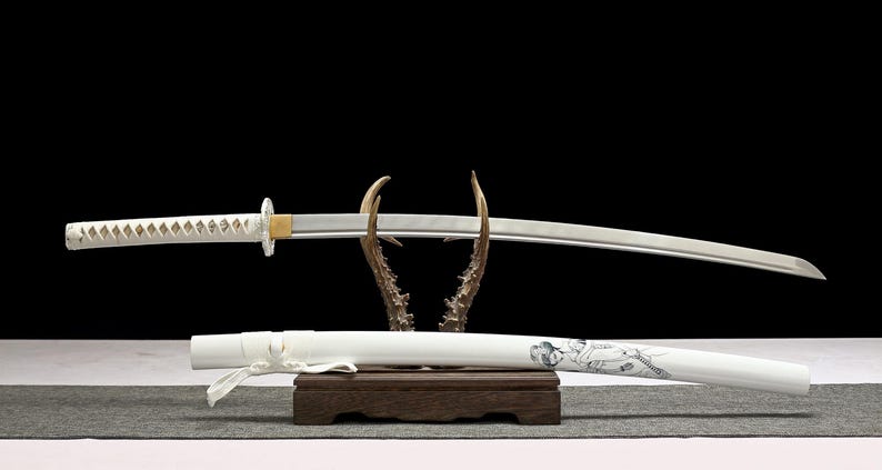A white katana sword with a white hilt and a white scabbard with a geisha design rests on a wooden antler stand.