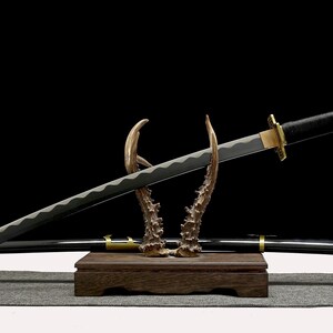 A black and gold katana with a silver blade rests on an antler-like stand, with its matching scabbard visible behind it.