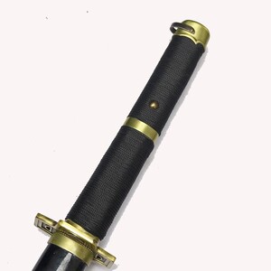 A close-up of the katana's black textured hilt with gold accents and a gold pommel.