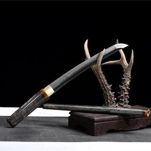 May include: A black and silver katana sword with a wooden handle and a black scabbard. The sword is displayed on a wooden stand with two antlers.