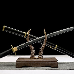 Two black and gold katana swords with silver blades are crossed on a wooden stand with antler-like supports.