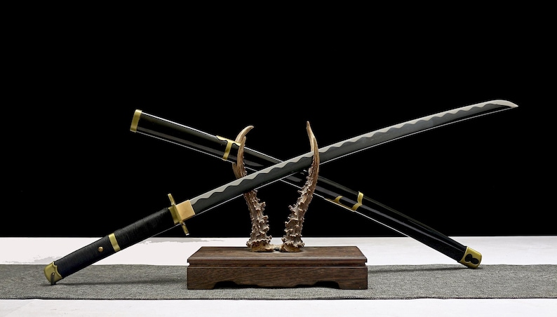 Two black and gold katana swords with silver blades are crossed on a wooden stand with antler-like supports.
