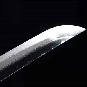 Close-up of a shiny silver katana blade tip, showing a subtle wavy pattern in the metal.
