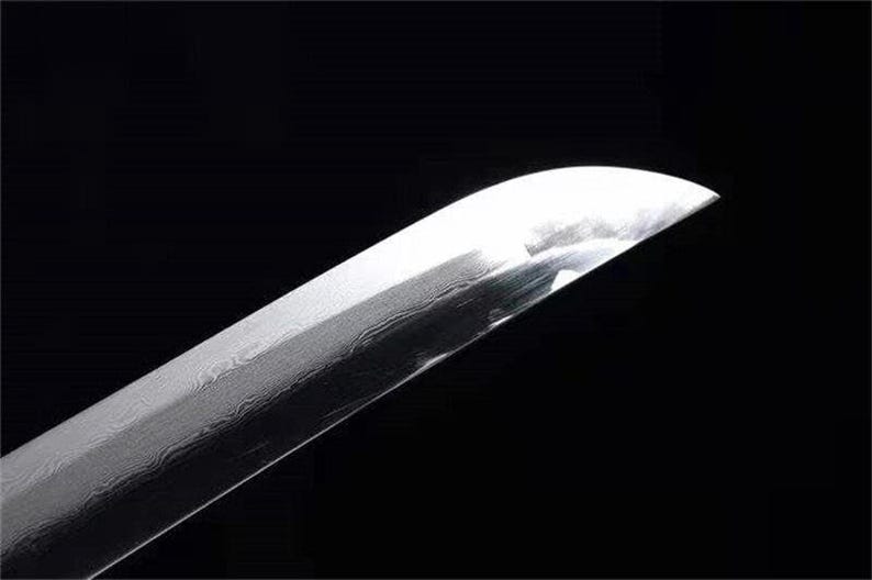 Close-up of a shiny silver katana blade tip, showing a subtle wavy pattern in the metal.