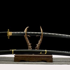 A black and gold katana with a silver blade rests on an antler-like stand, with its matching scabbard below.