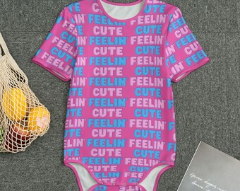 Könnte beinhalten: Ein rosa Baby-Body mit kurzen Ärmeln und einem runden Ausschnitt. Der Body ist mit einem sich wiederholenden Muster der Wörter "FEELIN' CUTE" in Blau und Rosa bedeckt. Das Kleidungsstück ist aus weichem Material.