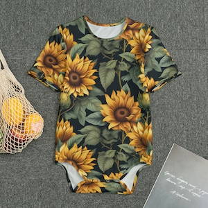 Pode incluir: Um body preto com estampa de girassóis. O body tem mangas curtas e um decote redondo.