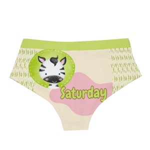 May include: Cream-colored underwear with a green waistband and a cartoon zebra face in a green circle. The word "Saturday" is written in pink and green on the front. The sides have a green and cream pattern.