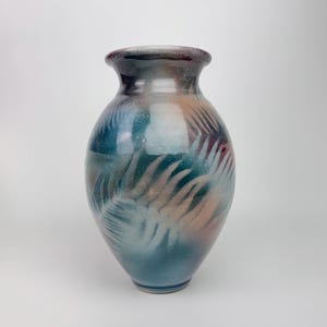 May include: A ceramic vase with a wide body and a narrow neck. The vase is painted with a gradient of colours, including blue, teal, peach, and burgundy. The design features a fern-like pattern. The vase is approximately 25 cm tall.