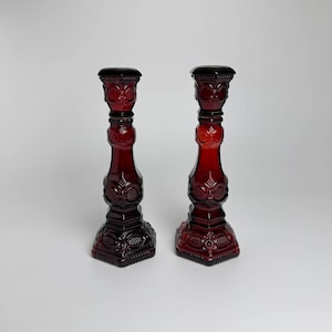 Puede incluir: Dos candelabros de vidrio rojo con un diseño detallado y ornamentado. Los candelabros son altos y delgados con una base redonda.