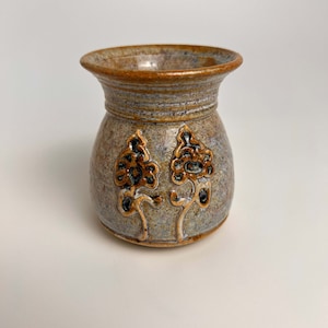 May include: A small, round, ceramic vase with a light brown glaze and gold leaf accents. The vase has a wide mouth and a narrow base. It features a floral design with two stylised leaves.