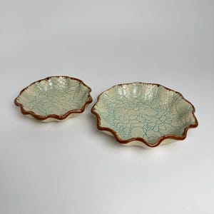 May include: Two ceramic bowls with a scalloped edge and a light blue and white floral design. The bowls have a brown rim.