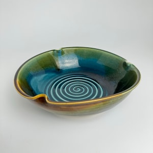 Puede incluir: Un tazón grande de cerámica con un esmalte azul oscuro y un patrón de espiral en el centro. El tazón tiene un esmalte verde y marrón en el exterior.