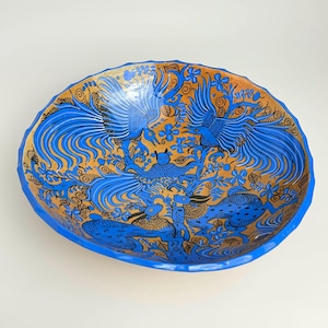 May include: A blue ceramic bowl with a gold rim and intricate black and blue designs of birds and animals. The bowl is decorated with a floral pattern.