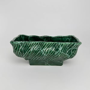 Op de afbeelding: Een groene keramische plantenbak met een marmeren afwerking en een vierkante basis. De plantenbak heeft een golvend, getextureerd ontwerp.