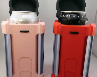 Puede incluir: Dos enfriadores de latas impresos en 3D, uno rosa y otro rojo, con tapas negras y porta latas plateados. Las tapas están abiertas y cada enfriador contiene una lata de bebida.