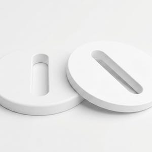 May include: Two white, circular objects with a recessed, elongated slot. The objects are positioned on a white surface, with one slightly overlapping the other. The design is minimalist and modern, with a clean, monochromatic aesthetic.