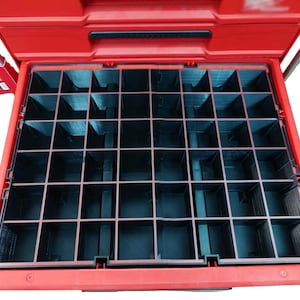 Puede incluir: Caja de herramientas roja abierta con un organizador de compartimentos negro y rojo. El organizador tiene múltiples compartimentos cuadrados y rectangulares para guardar piezas pequeñas y herramientas. La caja de herramientas está abierta, revelando el interior.