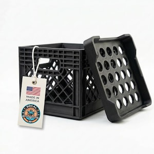 Peut inclure: Une petite caisse noire avec un couvercle amovible. La caisse présente un motif en treillis et une étiquette indiquant "MADE IN AMERICA" avec un drapeau américain et un logo. Le couvercle comporte plusieurs trous circulaires.