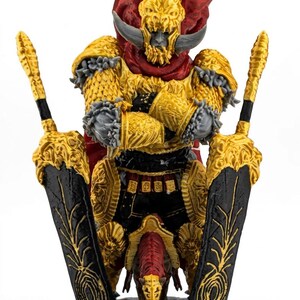 May include: A detailed figurine of a warrior in gold armor, red cape, and black and gold swords. The figure has a horned helmet and is posed with two large swords. The base is dark gray.