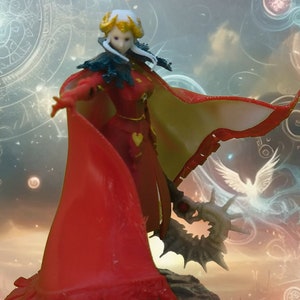 May include: A figurine of a character in a red dress and cape, with a gold heart detail. The figure has white hair and a dark green collar. The cape has a cream-colored lining. The figure is standing on a dark gray base.