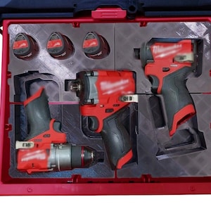 Puede incluir: Una caja de transporte de herramientas roja y negra con un inserto de espuma para guardar cuatro baterías, un taladro, un destornillador y una llave. Las herramientas son todas de la marca Milwaukee.