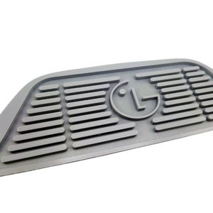 Puede incluir: Alfombra de goma gris con una superficie texturizada en relieve y un logotipo LG circular en el centro.