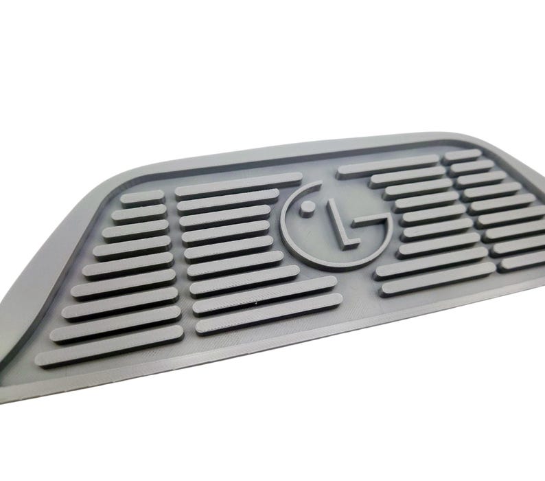 Puede incluir: Alfombra de goma gris con una superficie texturizada en relieve y un logotipo LG circular en el centro.