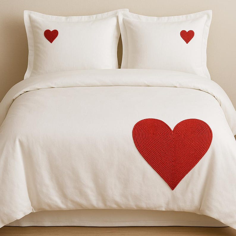 May include: A white bedding set consisting of a duvet cover and two pillowcases. The duvet cover features a large, textured red heart appliqu&eacute; on the lower right side, while each pillowcase displays a smaller, solid red heart embroidery.