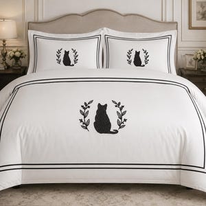 Pu&ograve; includere: Un copripiumino bianco e due federe abbinate con la sagoma ricamata in nero di un gatto seduto all'interno di una corona di foglie. Il set di biancheria da letto &egrave; decorato con un doppio bordo nero sul copripiumino e sulle federe.