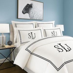 Puede incluir: Juego de cama blanco con ribete negro e iniciales monogramadas. El juego incluye una funda nórdica y fundas de almohada. Un retrato de oveja en blanco y negro enmarcado cuelga sobre la cama. La habitación tiene paredes azul claro.