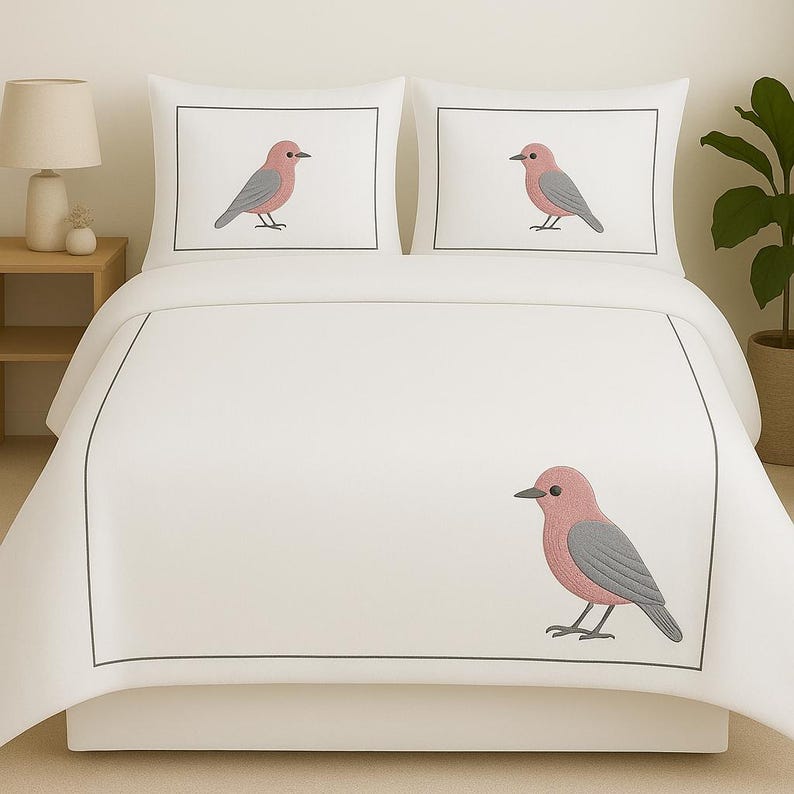 Puede incluir: Un juego de cama blanco que consta de una funda n&oacute;rdica y dos fundas de almohada, cada una con un borde rectangular gris fino y una ilustraci&oacute;n bordada de un p&aacute;jaro rosa y gris, centrado en las almohadas y en la funda n&oacute;rdica.