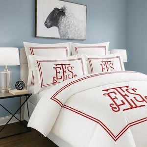 May include: White bedding set with red trim and embroidered initials. The set includes pillowcases and a duvet cover. A framed black and white sheep portrait hangs above the bed, creating a classic and elegant bedroom aesthetic.