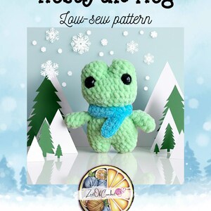 May include: A crocheted green frog with a blue scarf, titled "Frosty the Frog." The frog has large black eyes and is surrounded by paper snowflakes and Christmas trees. The image includes the text "Low-sew pattern" and a logo.
