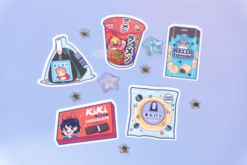 May include: A collection of anime-themed stickers featuring food items and characters. Includes a ramen cup, a Hello Totoro snack box, a Kiki's Chocolate box, and an onigiri sticker. Scattered star-shaped embellishments add a whimsical touch.