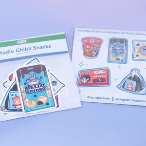 May include: Two packs of Studio Ghibli Snacks stickers. One pack features the text "Studio Ghibli Snacks" and includes stickers with the text "HELLO TOTORO". The other pack includes five die-cut stickers of snacks, with the text "ACUACL CHOCOLATE" and "ラーメン".