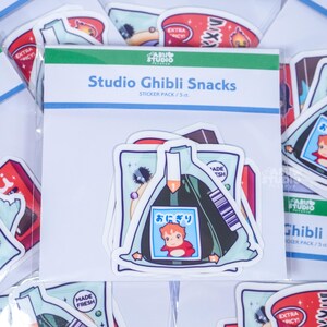 May include: A pack of Studio Ghibli Snacks stickers featuring various food-themed designs. The central pack displays an onigiri sticker with a cartoon character. Other stickers include ramen and other Japanese snacks.