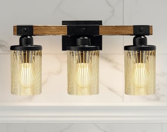May include: A three-light vanity fixture featuring a horizontal wooden beam mounted to a black rectangular backplate. Three cylindrical glass shades with vertical etched lines hang from black metal hardware, each housing a glowing light bulb.