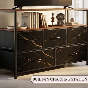 May include: A storage console with a black metal frame and a wooden top shelf. It features five fabric drawers with a black and gold marble pattern and black handles. The unit includes a built-in charging station, with books and decorative items displayed on the top surface.
