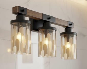 May include: A three-light vanity fixture with a dark wood and black metal frame. The light fixtures have clear glass shades with a pattern of white and tan shapes. The fixture is mounted on a white marble-look wall.