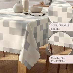 May include: A rectangular tablecloth featuring a geometric pixelated pattern in shades of cream, light gray, and dark gray. The fabric has a soft texture and is finished with a decorative scalloped edge detail along the entire perimeter.