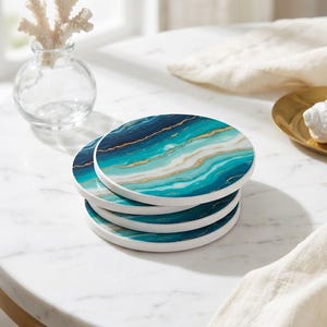 May include: A stack of four round coasters featuring a marbled pattern in shades of teal, navy blue, and white, accented with thin, wavy gold lines. Each coaster has a smooth, white edge and a flat, circular surface design.