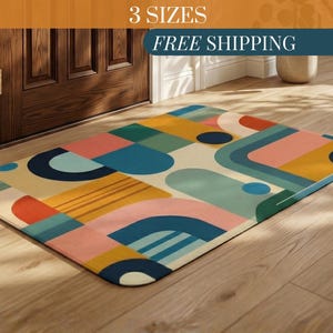 May include: A rectangular floor mat featuring a geometric pattern of overlapping shapes in shades of teal, mustard yellow, coral pink, and dark blue on a cream background. The text 3 SIZES and FREE SHIPPING is visible at the top of the image.