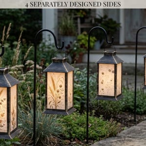 May include: Four outdoor lanterns with black distressed metal frames hanging from black shepherd hooks. Each lantern features four separately designed sides with botanical illustrations of wheat and wildflowers, illuminated from within.
