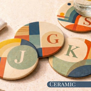 May include: Four ceramic coasters with colorful geometric designs and letters: J, G, K, and S. The coasters have a cork base and a cream-colored surface with blue, orange, and yellow accents. The word "CERAMIC" is printed on a blue banner.